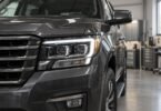 Close-up of a dark gray SUV headlamp with a white light strip and amber side marker in a workshop.