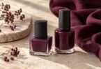 Two unbranded bottles of plum and wine-colored nail polish on pale stone beside burgundy fabric