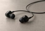 Two unbranded black wired earbuds with silicone tips and a loosely curved cable on a neutral tabletop.