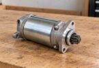 An unbranded detached small-engine starter motor with a visible pinion resting on a wooden workbench.