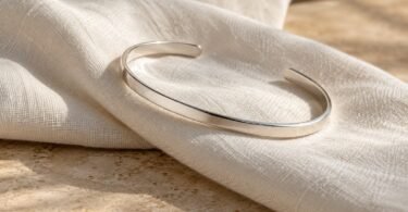 A plain silver-tone open cuff bracelet resting on folded ivory linen.