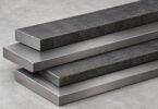 Illustration of plain rectangular steel bars stacked on a gray surface.