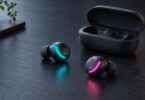Illustration of two unbranded earbuds with cyan and magenta lights beside an open charging case