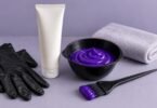 Purple color cream in a black tint bowl beside an unbranded tube, tint brush, gloves and folded towel.