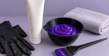 Purple color cream in a black tint bowl beside an unbranded tube, tint brush, gloves and folded towel.