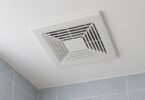 Illustration of a generic white bathroom ventilation grille on a pale ceiling above blue-gray tiled walls