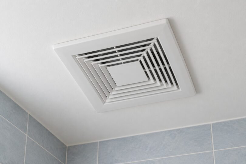Illustration of a generic white bathroom ventilation grille on a pale ceiling above blue-gray tiled walls