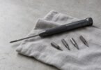 Illustrative unbranded precision screwdriver and four loose driver bits arranged on a gray cloth