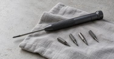 Illustrative unbranded precision screwdriver and four loose driver bits arranged on a gray cloth