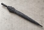Illustration of a closed unbranded charcoal umbrella on a pale tabletop with water droplets