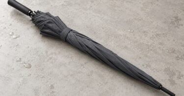 Illustration of a closed unbranded charcoal umbrella on a pale tabletop with water droplets