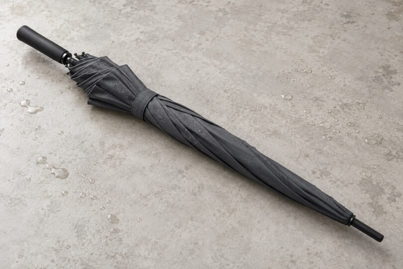 Illustration of a closed unbranded charcoal umbrella on a pale tabletop with water droplets