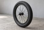 Illustration of unbranded black BMX-style tire mounted on a spoked wheel against a gray workshop wall