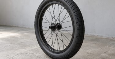 Illustration of unbranded black BMX-style tire mounted on a spoked wheel against a gray workshop wall