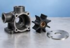Illustration of an unbranded dark pump housing beside a black impeller and circular metal wear plate on a gray surface.