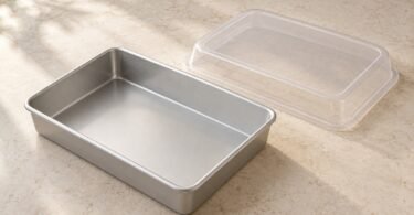 Illustrative unbranded rectangular metal cake pan with a separate clear storage lid on a pale countertop