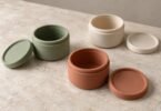 Three empty green, terracotta and cream silicone containers with their lids beside them on a pale stone tabletop.