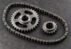 Illustration of a generic roller chain and two separate steel sprockets on a dark workshop surface.