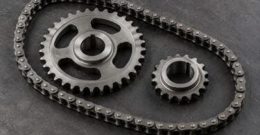 Illustration of a generic roller chain and two separate steel sprockets on a dark workshop surface.