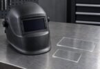 Illustration of an unbranded welding helmet and two clear protective lens covers on a workbench.