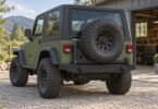 Generic illustration of an olive two-door off-road vehicle with a black rear bumper and closed swing-out spare tire carrier outside a workshop.