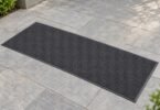 Illustrative unbranded charcoal entry mat lying flat on pale outdoor stone pavers.