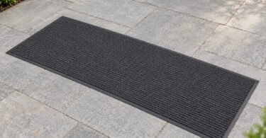 Illustrative unbranded charcoal entry mat lying flat on pale outdoor stone pavers.