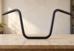 An unbranded black ape-hanger motorcycle handlebar standing on a pale wooden workbench.
