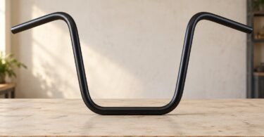 An unbranded black ape-hanger motorcycle handlebar standing on a pale wooden workbench.