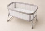 Illustration of an empty mesh-sided bassinet with a flat white sleep pad on a level floor