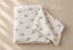 Folded ivory fabric blanket with small gray elephant prints and one corner spread out on a beige surface.