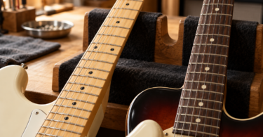 Two electric guitar necks with pale and dark fingerboards resting on padded supports in a workshop.