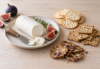 Goat cheese, figs and three styles of crackers arranged on a wooden table.