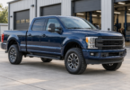 A dark blue crew-cab pickup parked on level concrete outside an automotive workshop.