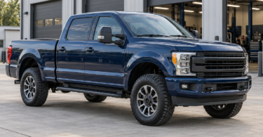A dark blue crew-cab pickup parked on level concrete outside an automotive workshop.