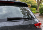 A black rear wiper rests on a rain-speckled SUV window.