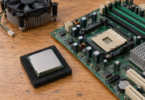 A generic desktop processor on a black foam pad beside an older motherboard and a separate CPU cooler.