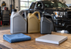 Three unbranded oil jugs, a folded cloth and a closed booklet on a garage workbench with a pickup behind them.