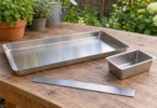 A shallow metal tray and separate small catch cup on a wooden outdoor workbench