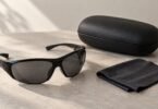 Unbranded black wraparound sunglasses with grey lenses beside a black case and folded cleaning cloth