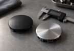 Unbranded black and silver round wheel center caps beside a digital caliper on a gray workbench