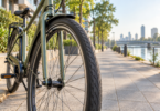 Close view of a black front tire and fender on an unbranded city bicycle beside a paved waterfront path.
