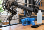 Bicycle chain and cassette beside a generic blue chain scrubber, blank bottle and brush on a wooden workbench