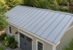 Pale gray standing-seam metal roof on a cream garden workshop surrounded by trees