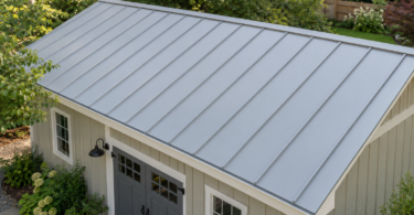Pale gray standing-seam metal roof on a cream garden workshop surrounded by trees