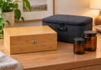 A closed bamboo box with a keyhole, a closed charcoal fabric case with a combination lock, and two empty amber jars on a wooden table.