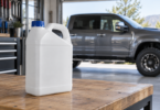 An unmarked white jug with a blue cap on a garage workbench, with a pickup truck behind it.