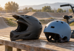 Charcoal full-face helmet and blue open-face helmet on a bench beside a BMX bicycle and dirt track