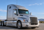 Silver semi-truck tractor parked outdoors with a vertical antenna beside its cab
