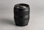Generic unbranded black camera zoom lens standing on a gray studio surface